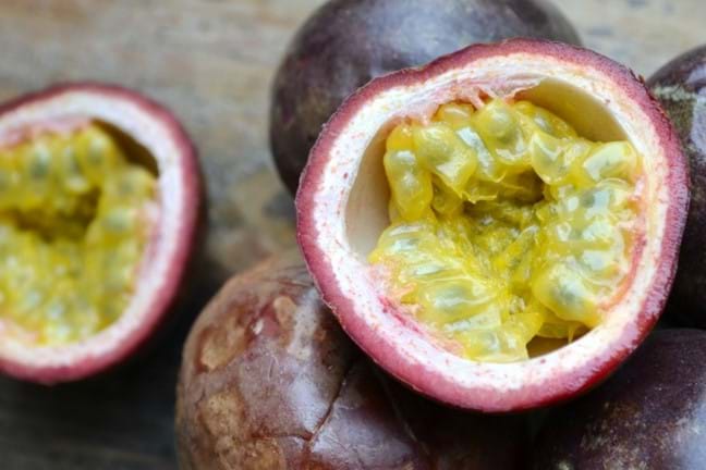 Black Passionfruit (passiflora edulis) harvested fruits, some have been cut in half exposing the yellow pulp inside.