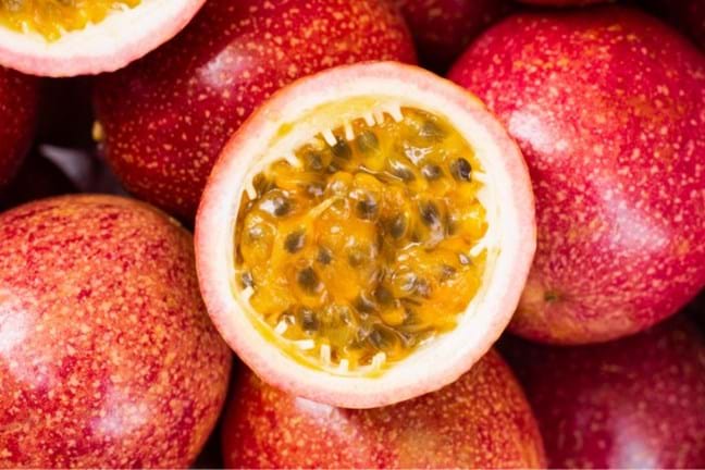 red passionfruit harvested fruits, some have been cut in half exposing the  orange pulp and black seeds inside.