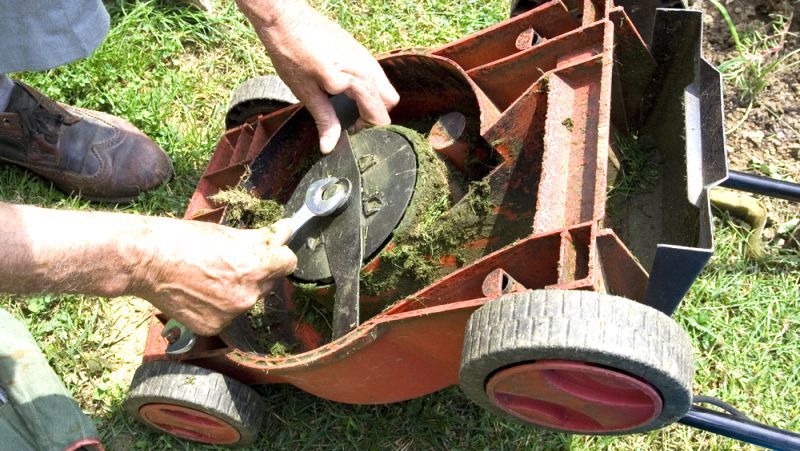 Man inspecting upside down mowers blades using a spanner