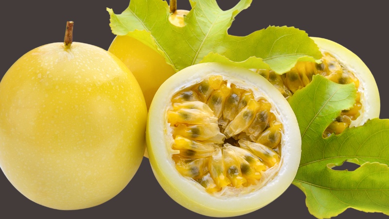 Yellow Passionfruit 2 leaves and harvested fruits, some have been cut in half exposing the yellow pulp and black seeds inside.