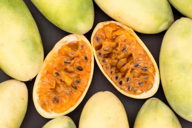 Banana Passionfruit (passiflora mollissima) harvested fruits, some have been cut in half exposing the orange pulp and black seedsinside.