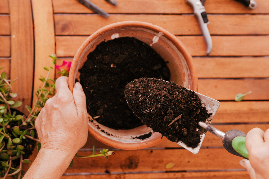 person filling a small terracotta pot with potting mix using a hand trowel