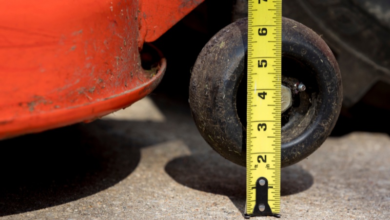 close up of a mower wheel being lifted and a measuring tape being held out and perpendicular to the ground - testing mower height