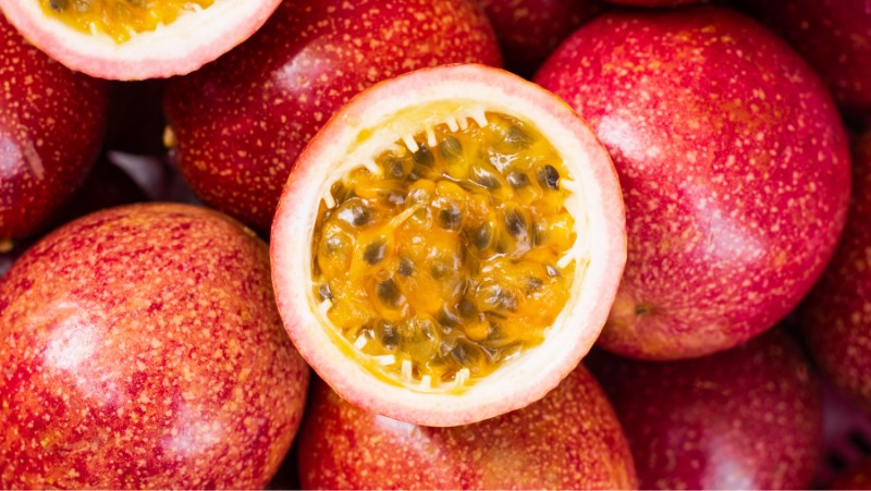 red passionfruit harvested fruits, some have been cut in half exposing the  orange pulp and black seeds inside.