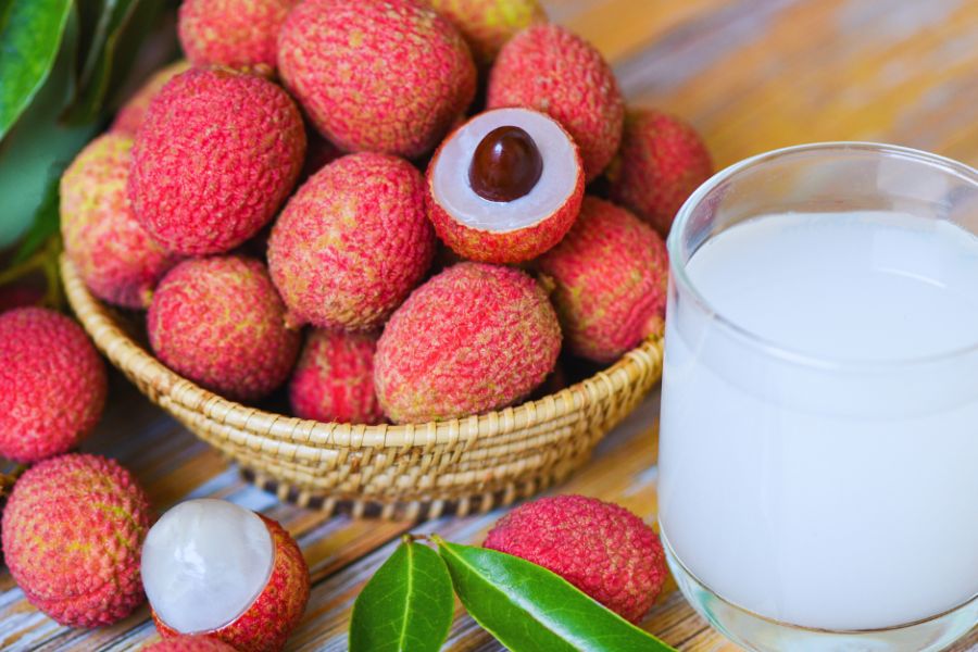 A bowl of lychee on a table with a couple unpeeled to reveal the seed and flesh