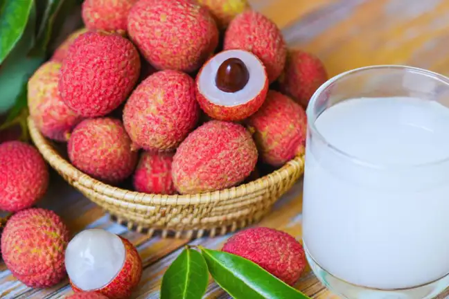 A bowl of lychee on a table with a couple unpeeled to reveal the seed and flesh