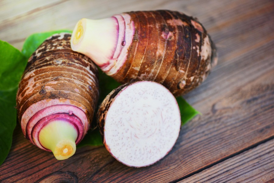 Taro corms whole and cut in half on a wooden chopping board
