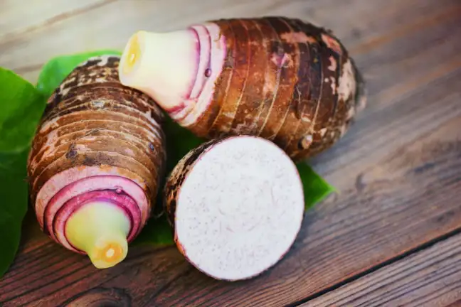 Taro corms whole and cut in half on a wooden chopping board