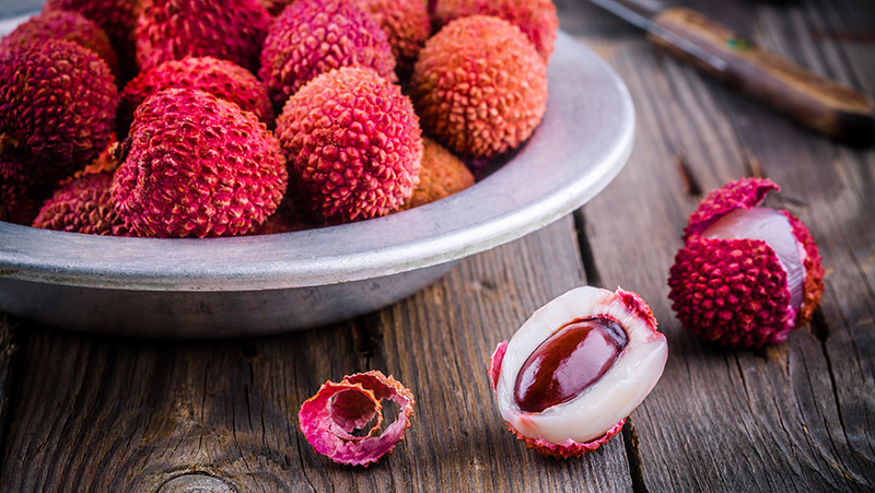 A bowl of lychee on a table with a couple of fruit unpeeled to reveal the flesh