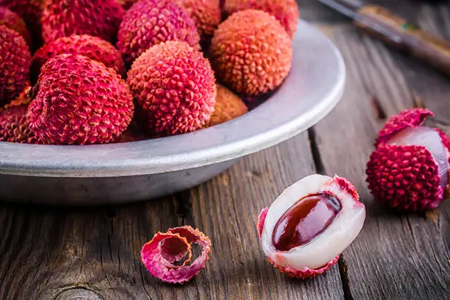 A bowl of lychee on a table with a couple of fruit unpeeled to reveal the flesh