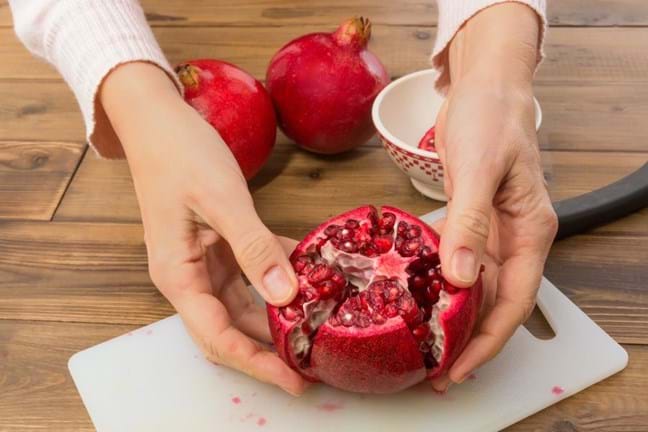Hands splitting open the cut segments on of a pomegranate