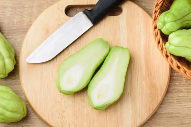 Choko sliced in half on a chopping board